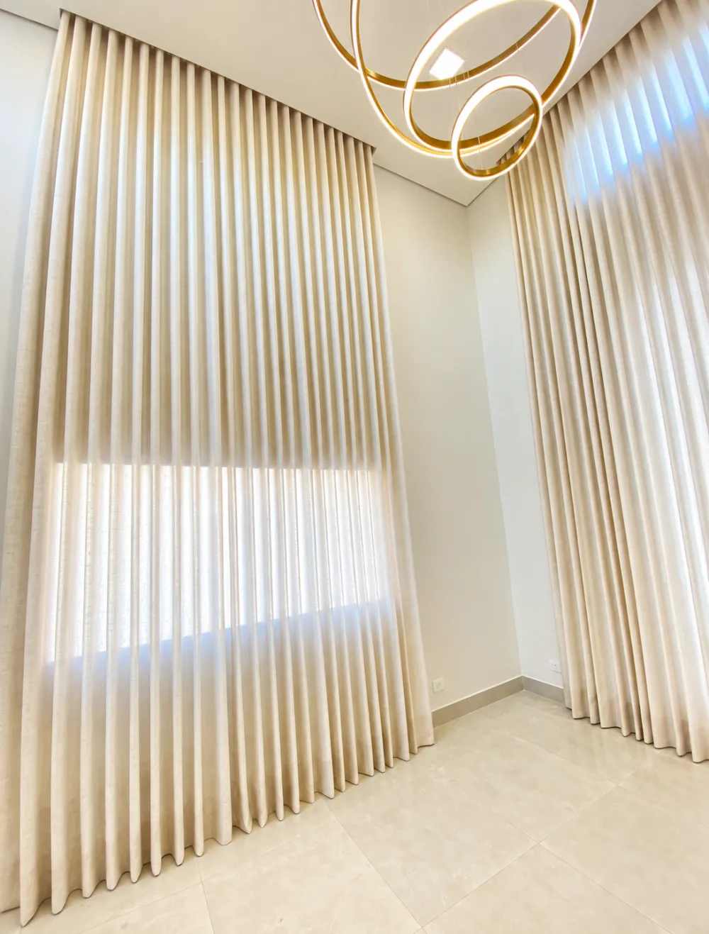 Sala de pé-direito duplo com cortina wave e lustre dourado